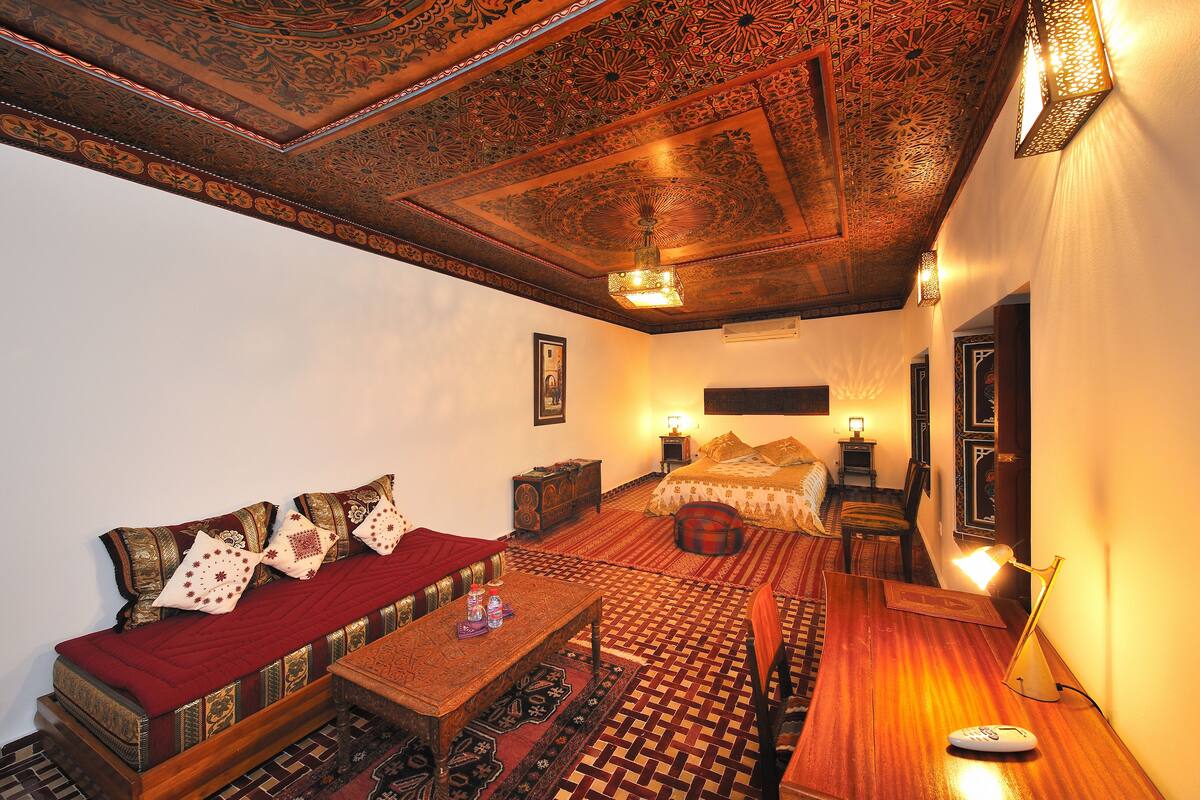 A traditional room with a sofa, a bed, a wooden table, and a patterned floor.