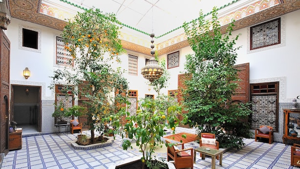 A traditional courtyard with tiled flooring, potted plants, and wooden furniture. - Riad Souafine (Fes)