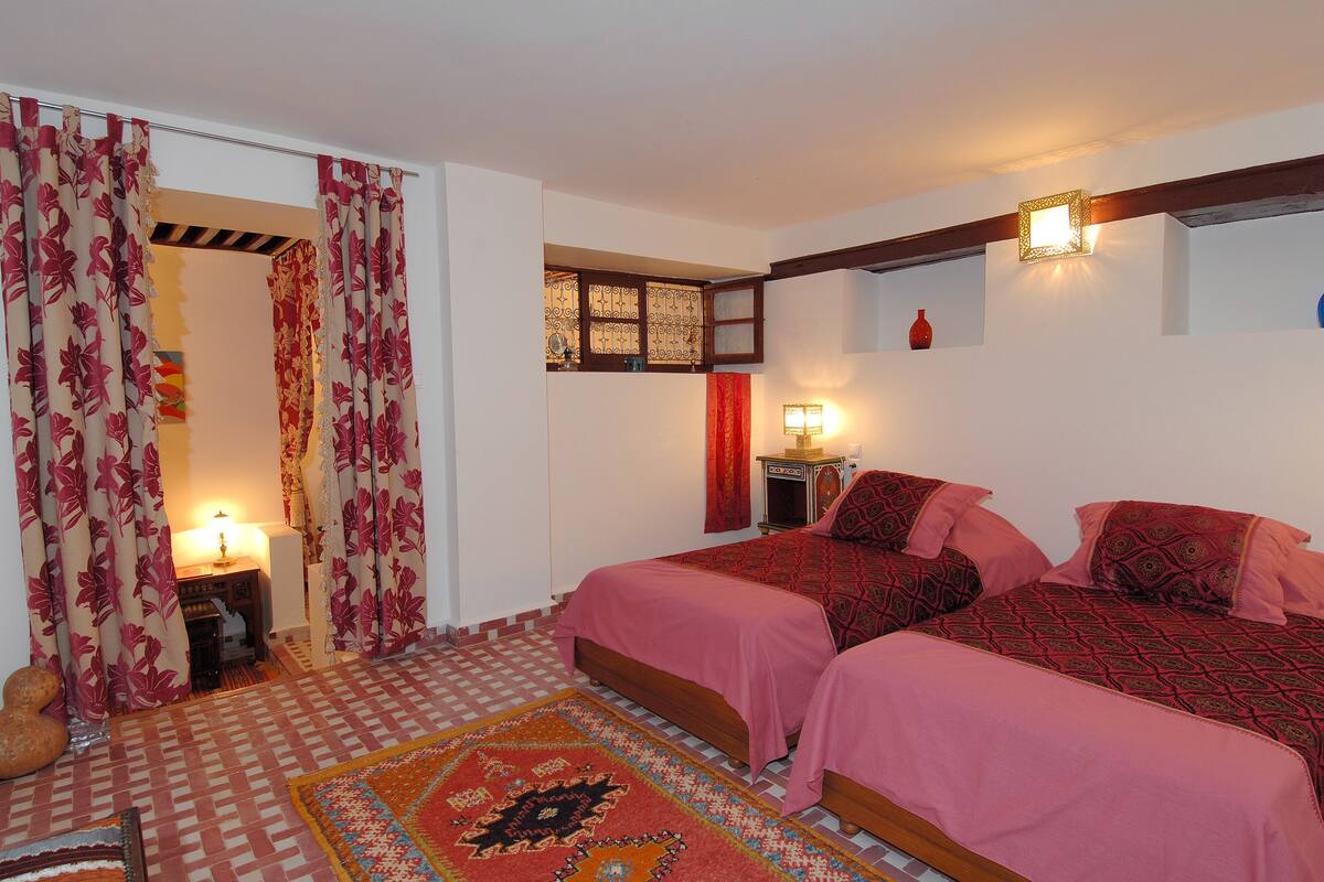 A bedroom with two beds, a patterned rug, a lamp, and a decorative wall piece.