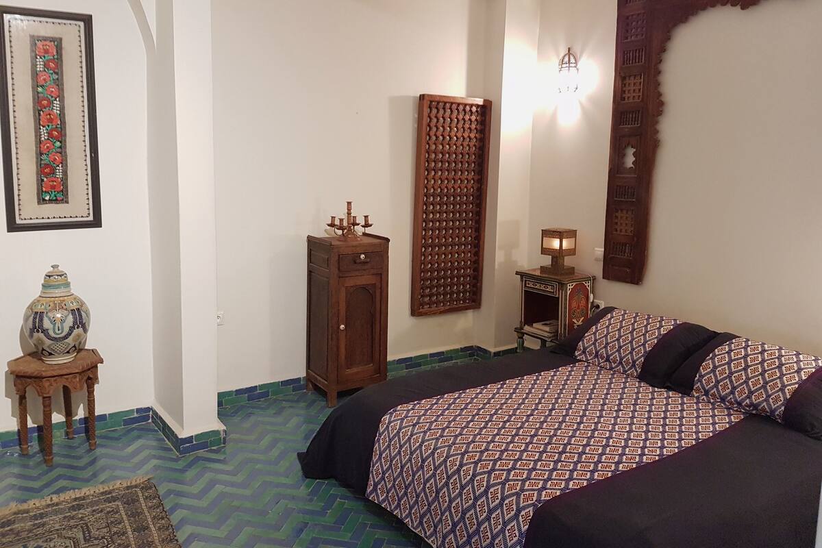 A bedroom with a bed, a wooden cabinet, a wall-mounted lamp, and a decorative panel.