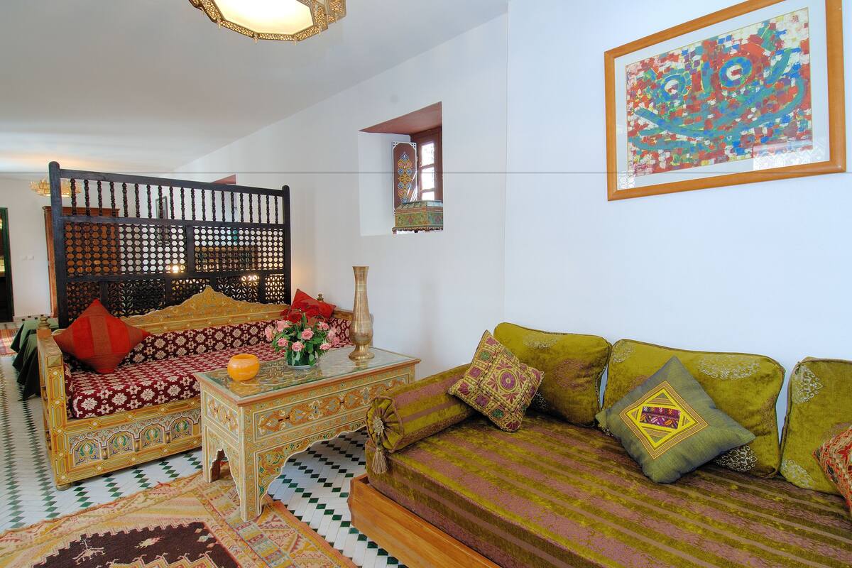 A traditional Moroccan-style living room with a patterned sofa, a wooden coffee table, and a decorative screen.