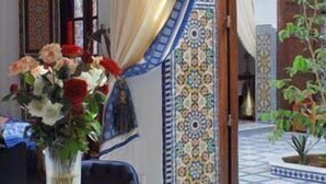A room with a table set for dining, a vase with flowers, and a view of a courtyard with a tiled floor and a plant. - Riad Souafine (Fes)