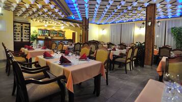 A restaurant with multiple tables set for dining, wooden chairs, and a bar area in the background.