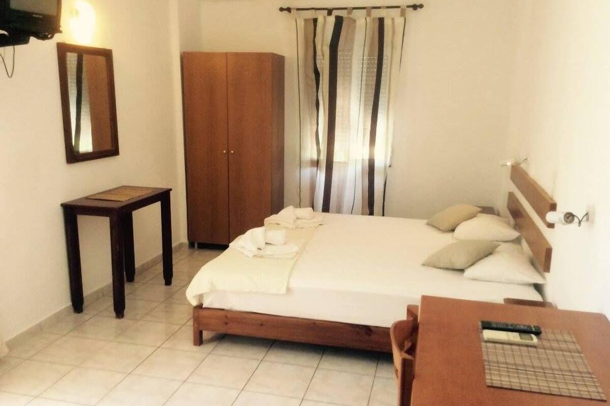 Une chambre à coucher avec un lit, une armoire en bois, une petite table et un miroir au mur.