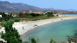 A beach with clear turquoise water, a castle in the background, and rocky terrain. - Maria's Studios (Sfakia)