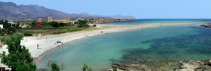 Una playa con agua turquesa cristalina, un castillo al fondo y terreno rocoso.