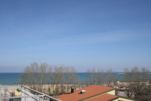 A coastal view with a clear sky, a beach, and a building with a red roof and green walls. - Hotel Gaston (Rimini)