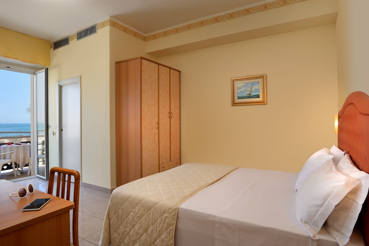Une chambre d’hôtel avec un lit, une armoire en bois, un bureau avec une tablette et des lunettes de soleil, et un tableau accroché au mur.