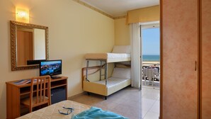 Une chambre d’hôtel avec un lit, un bureau avec un ordinateur, un lit superposé et un balcon donnant sur la mer.
