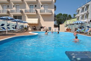 A swimming pool with lounge chairs and umbrellas, surrounded by a building with balconies. - Hotel Gaston (Rimini)