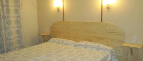 Un dormitorio con cabecera de madera, dos mesitas de noche y una colcha estampada.