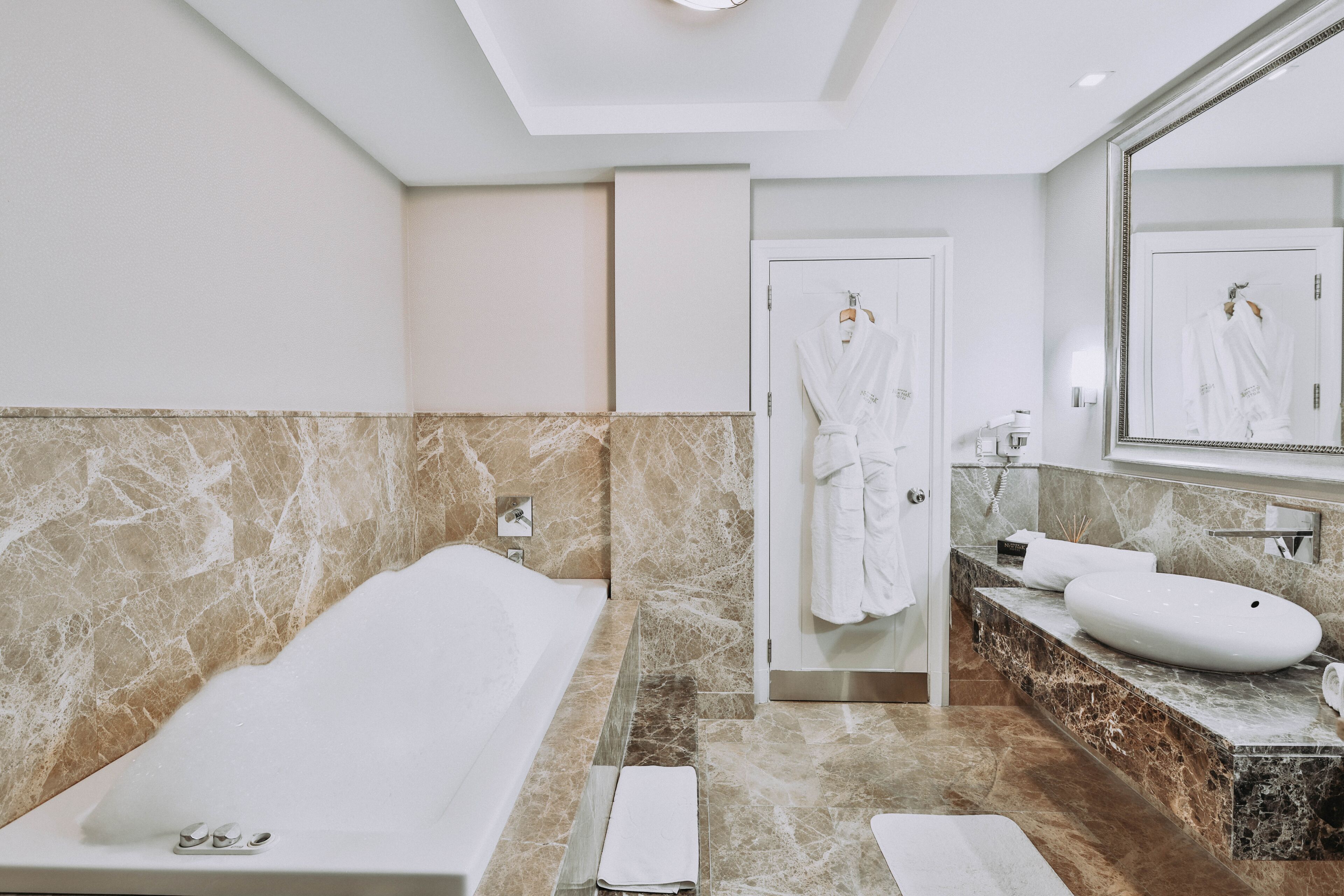 Un baño moderno con bañera, un espejo grande, tocador con lavamanos y una bata colgada en la puerta.