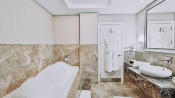 Un baño moderno con bañera, un espejo grande, tocador con lavamanos y una bata colgada en la puerta.