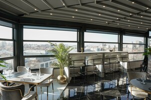 A modern dining area with a panoramic city view, a large plant, and a bar counter.
