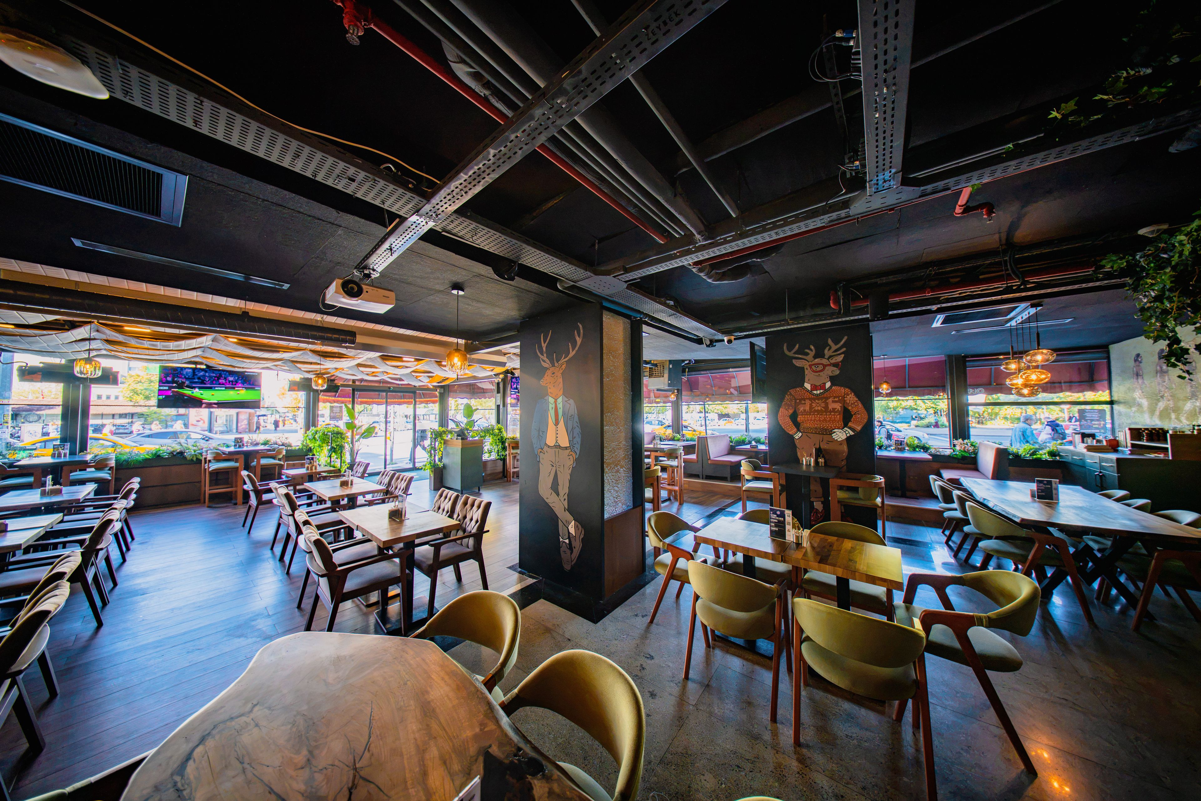 An indoor dining area with multiple tables and chairs, ceiling beams, and a mural on the wall.