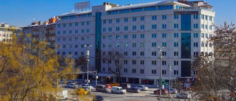 A multi-story hotel with a prominent sign, a parking lot, and surrounding trees.