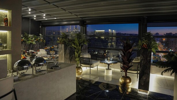 Un espacio lounge moderno con vista a la ciudad, que incluye un bar y diferentes disposiciones de asientos.