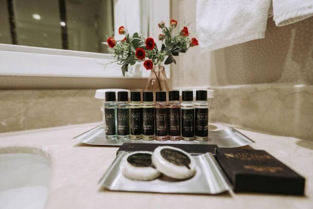 Ein Badezimmer-Waschtisch mit einer Reihe Parfumflaschen, einer Vase mit roten Blumen und einer Schale mit zwei Keksen.