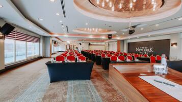 A conference room with rows of red chairs, a wooden table, and a large screen displaying "NEW PARK HOTEL".