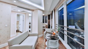 Una habitación de hotel moderna con sofá, mesa de comedor y ventanas grandes con vistas a la ciudad.