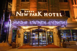 Exterior del Hotel New Park, con puerta giratoria, letrero iluminado y luces decorativas.