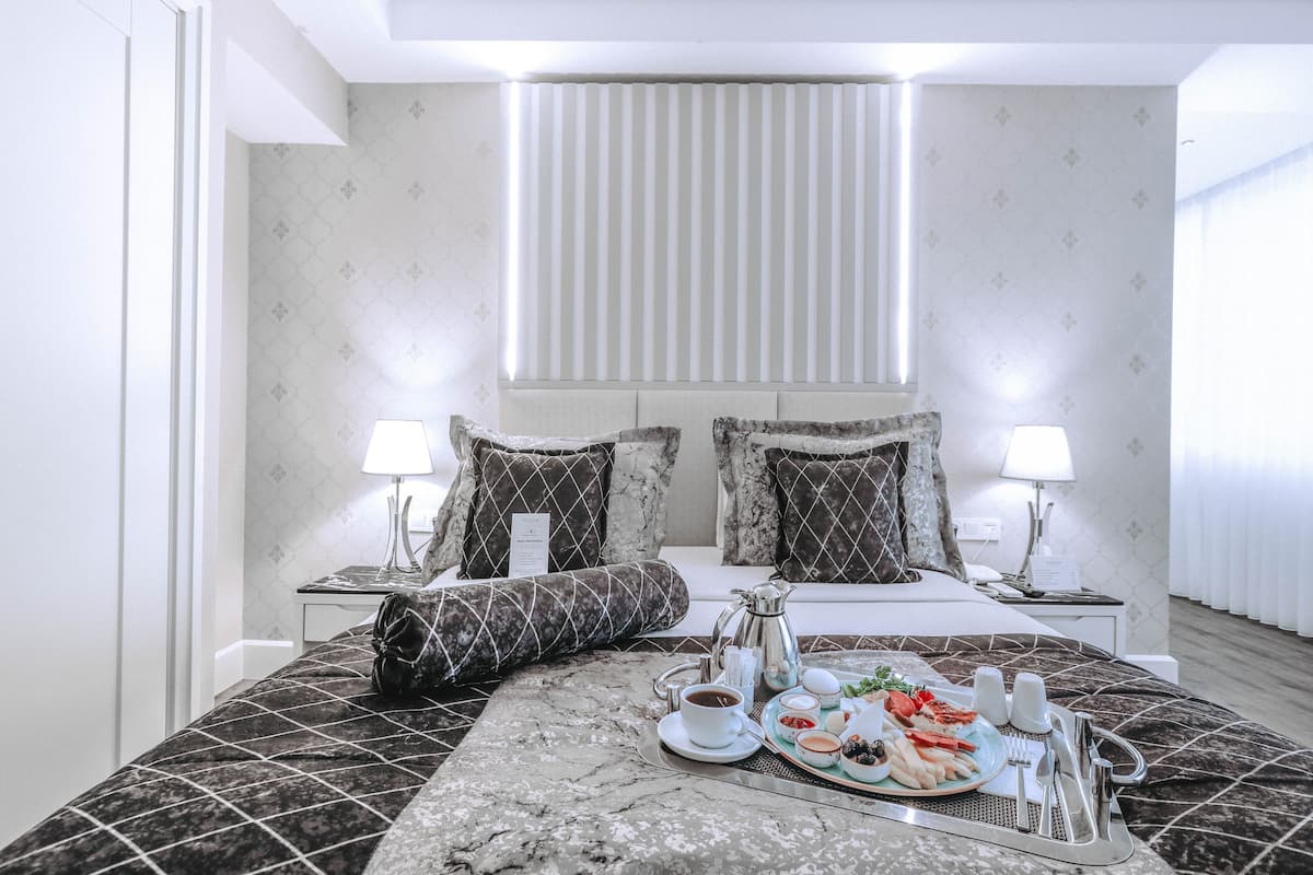 Ein Hotelzimmer mit einem aufgeräumten Bett, einem Frühstücksbrettchen auf dem Bett und einem Fenster mit Jalousien.