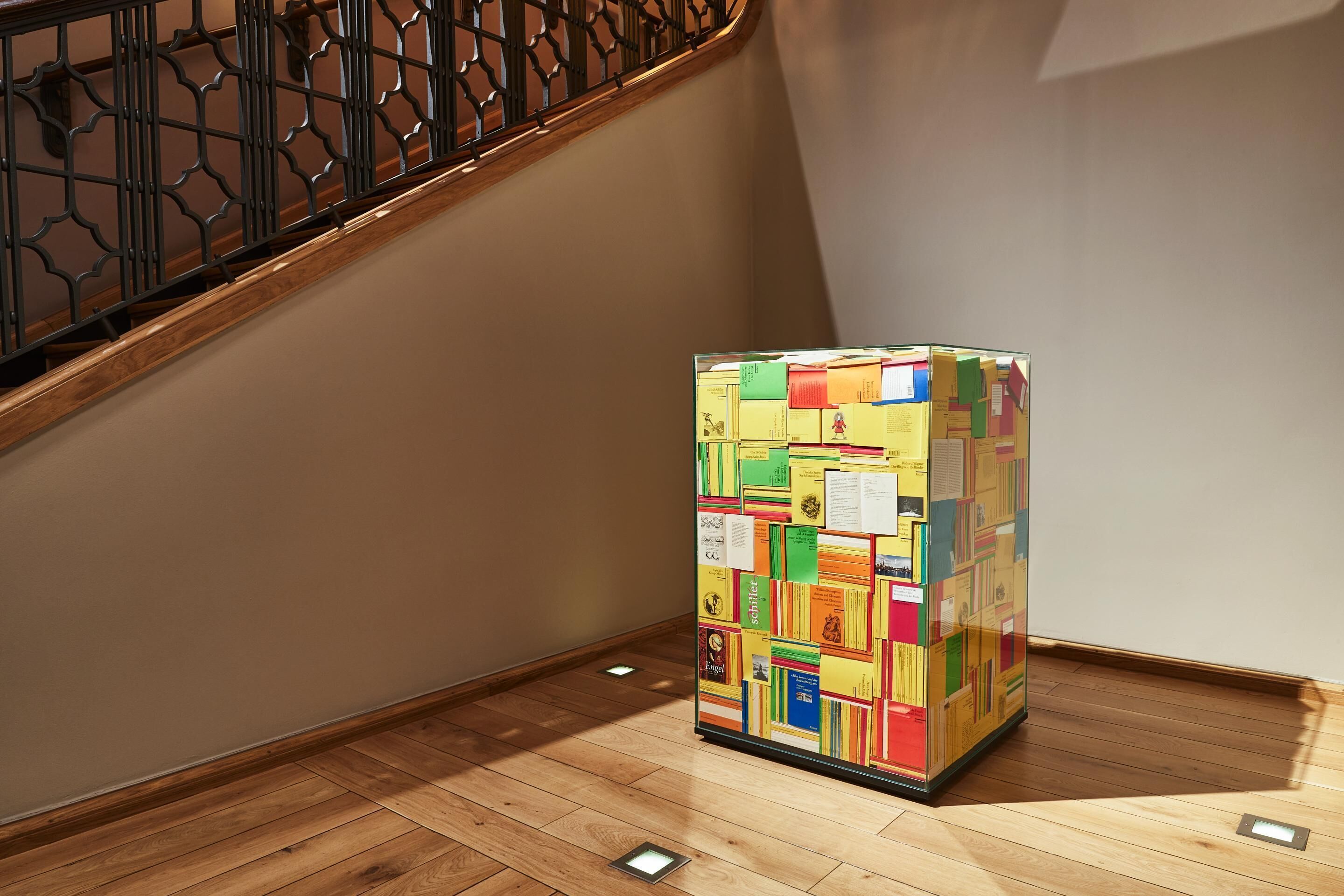 Una escalera con barandilla de madera y una pared con un tablón de anuncios lleno de colores.