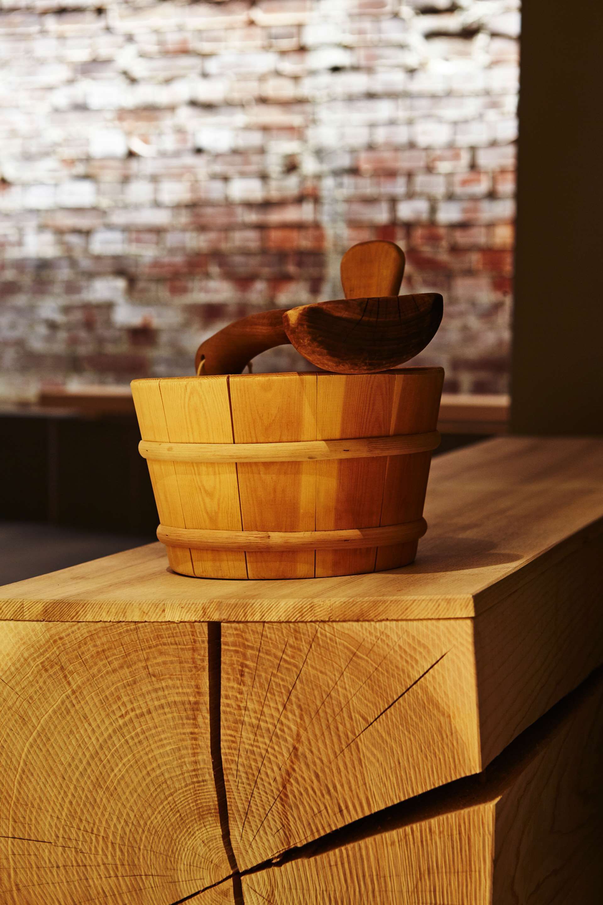 Un balde de madera con asa y una cuchara de madera descansando sobre una superficie de madera.