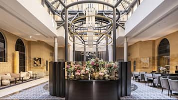 Un hall de hotel con un arreglo floral central, zonas de estar y una estructura de techo de vidrio.