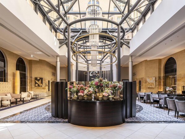 Un hall de hotel con un arreglo floral central, zonas de estar y una estructura de techo de vidrio.