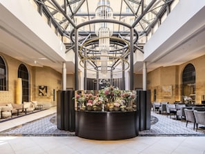 Un hall de hotel con un arreglo floral central, zonas de estar y una estructura de techo de vidrio.