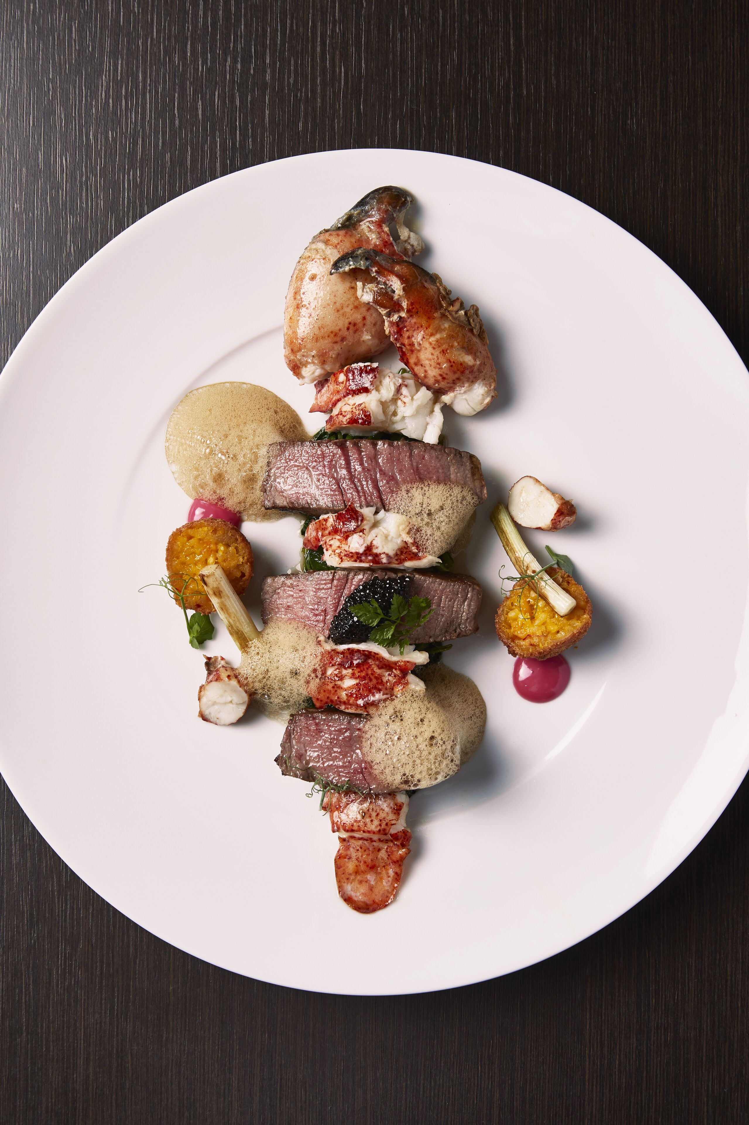 Un plato blanco con diversos alimentos, entre ellos carne, verduras y un objeto pequeño y redondo.