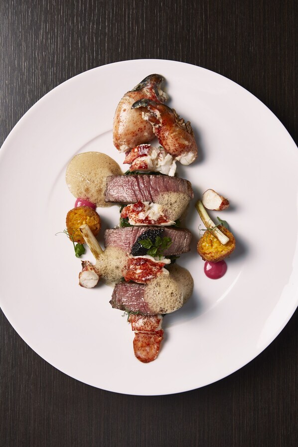 Un plato blanco con diversos alimentos, entre ellos carne, verduras y un objeto pequeño y redondo.