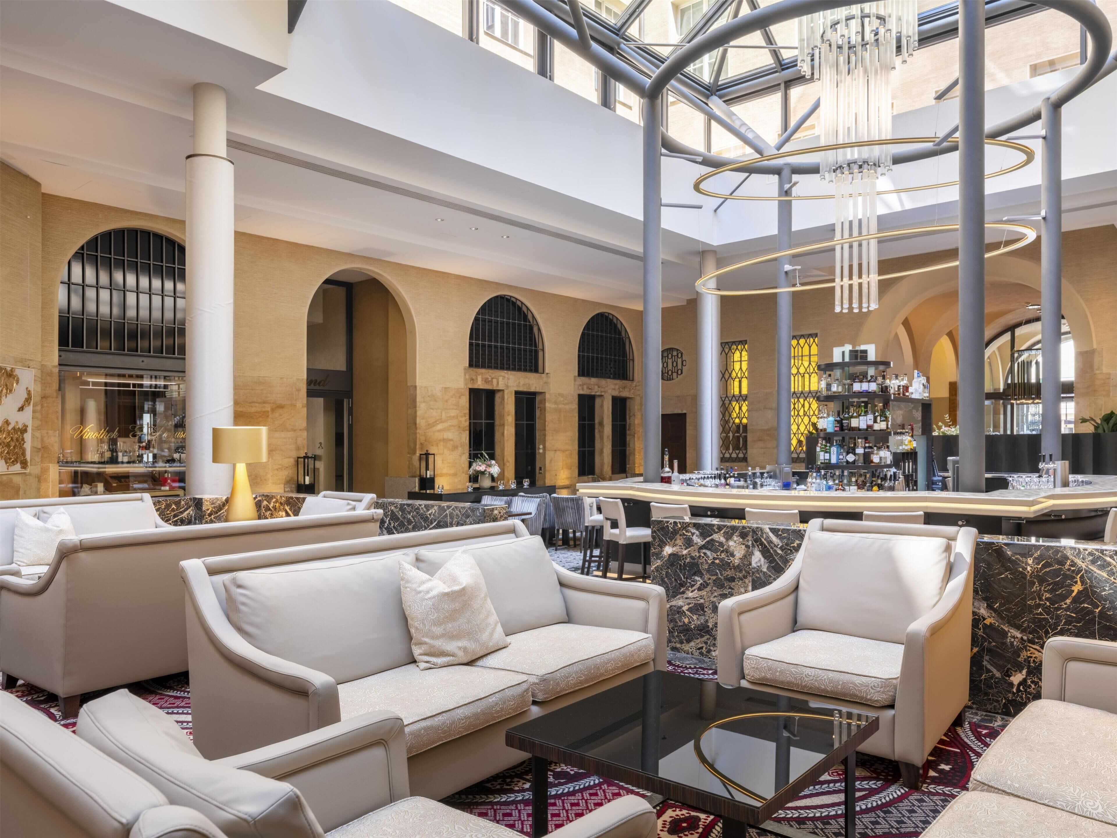 Eine geräumige Lobby mit Barbereich, Sitzgelegenheiten und einer hohen Decke mit einem modernen Kronleuchter.