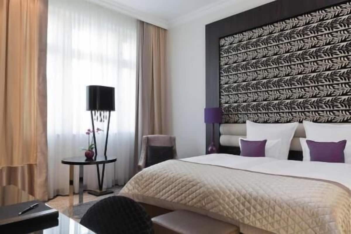 Une chambre d’hôtel avec un grand lit, une table de chevet, une lampe sur pied et une tête de lit à motifs.