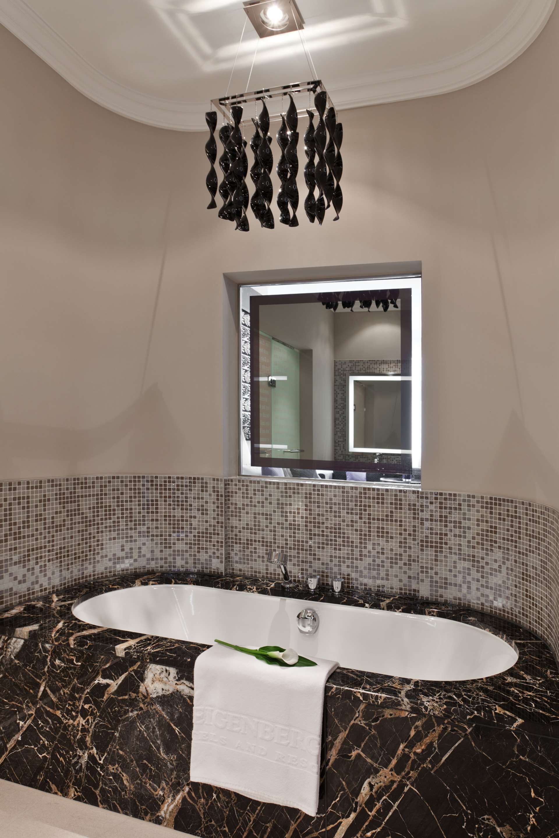 Un baño moderno con una bañera grande, una escultura abstracta negra colgante, una ventana con vistas y un salpicadero de azulejos.