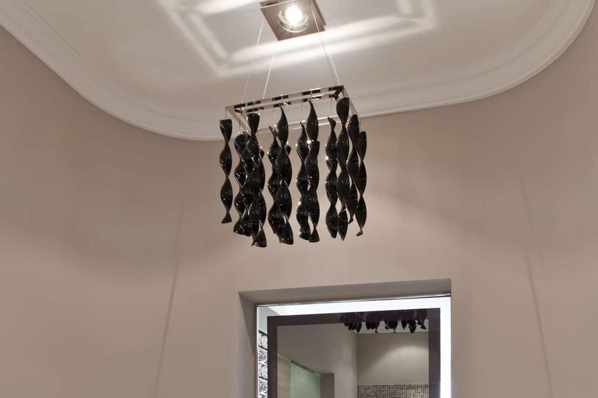Une salle de bain moderne avec une grande baignoire, une sculpture abstraite noire suspendue, une fenêtre offrant une belle vue et un mur recouvert de carreaux.