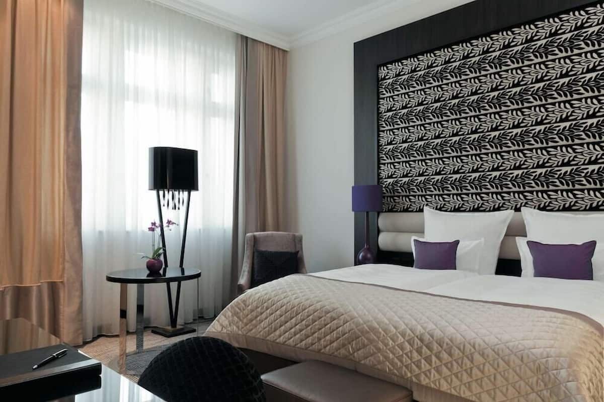 Une chambre d’hôtel avec un grand lit, une petite table de chevet, une chaise et une tête de lit décorative.