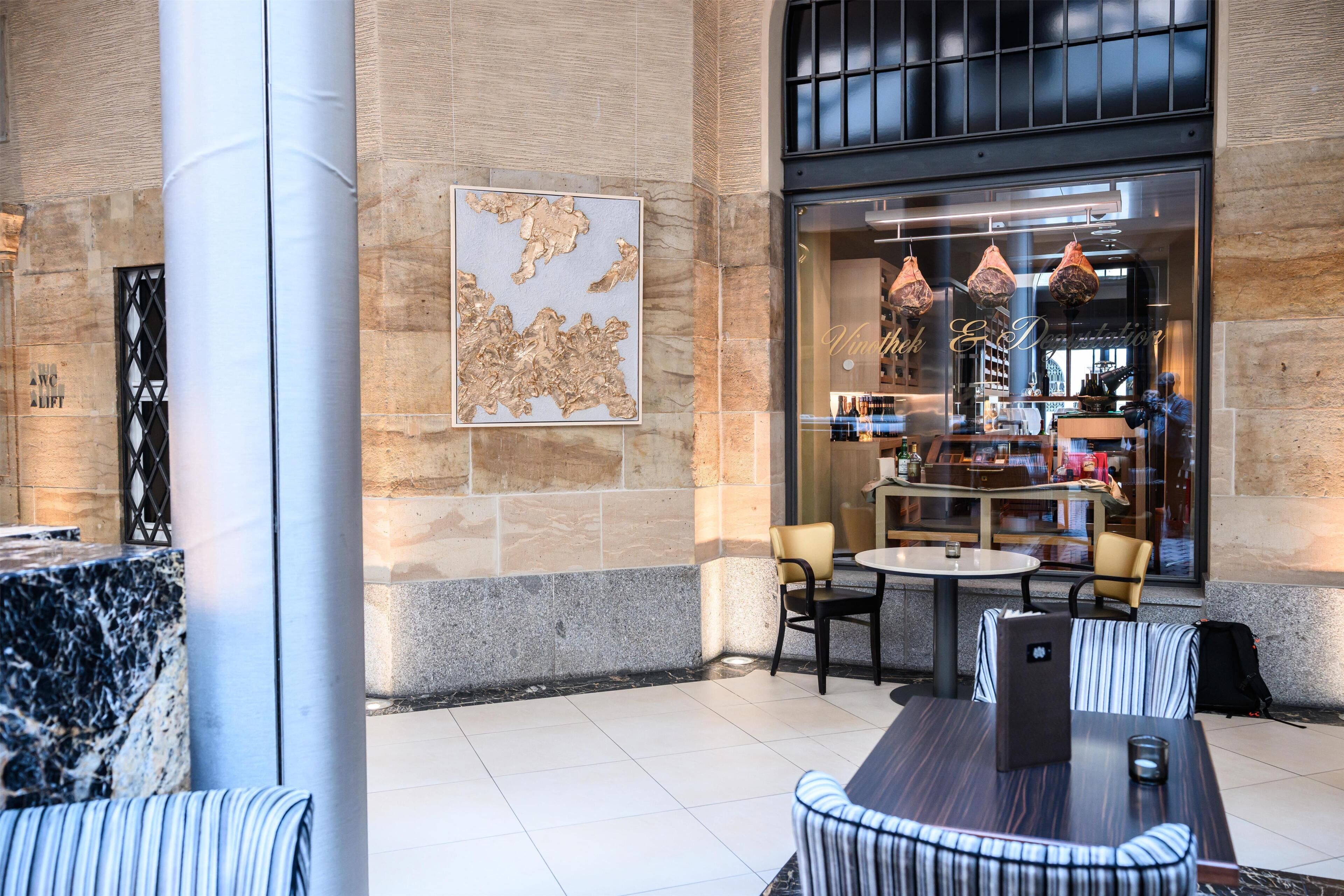 Een hotel lobby met marmeren zuilen, een grote decoratieve kaart en een zithoek met tafels en stoelen.