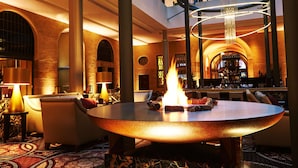 A lobby with a round table featuring a fire, seating, and a bar area.