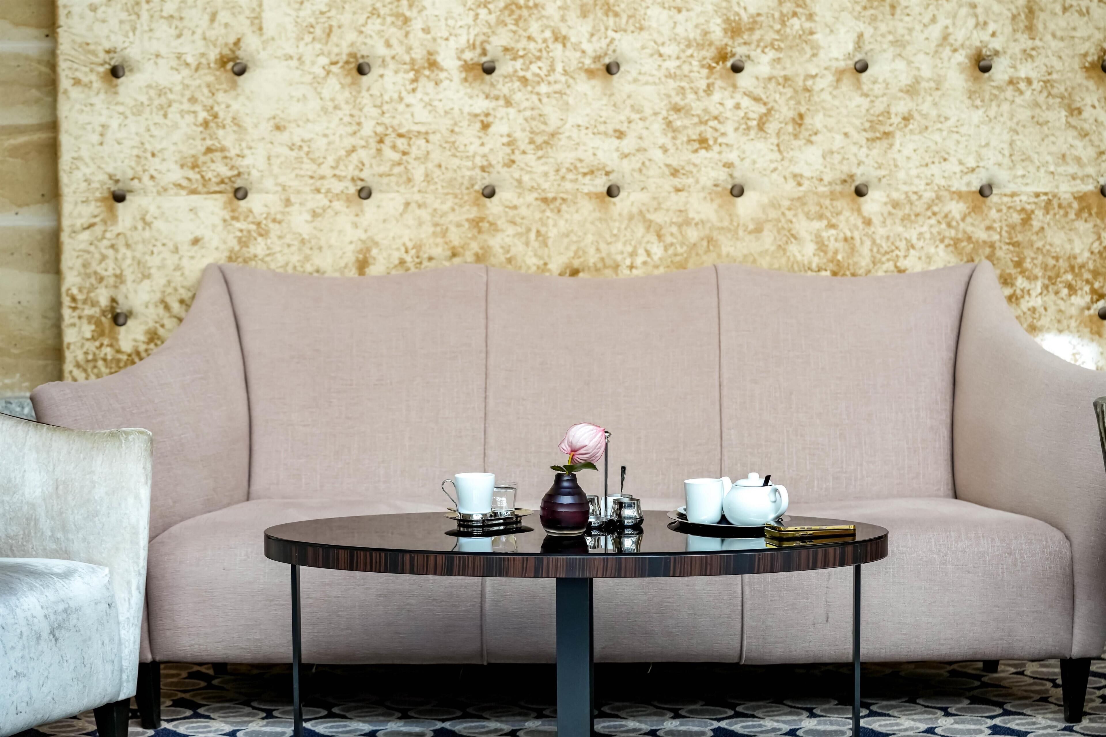 A sofa with a tufted backrest, a round table with a vase and teapots, and a patterned floor.