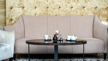 A sofa with a tufted backrest, a round table with a vase and teapots, and a patterned floor.