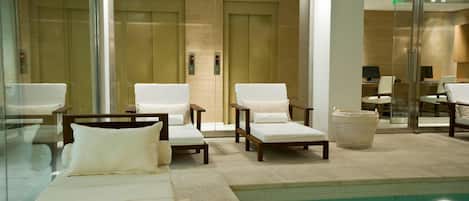 A hotel lobby with a swimming pool, lounge chairs, and an elevator.
