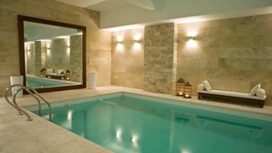 A modern indoor pool with a clear blue water, stone walls, and a bench with cushions. - Awwa Suites and Spa (Buenos Aires)