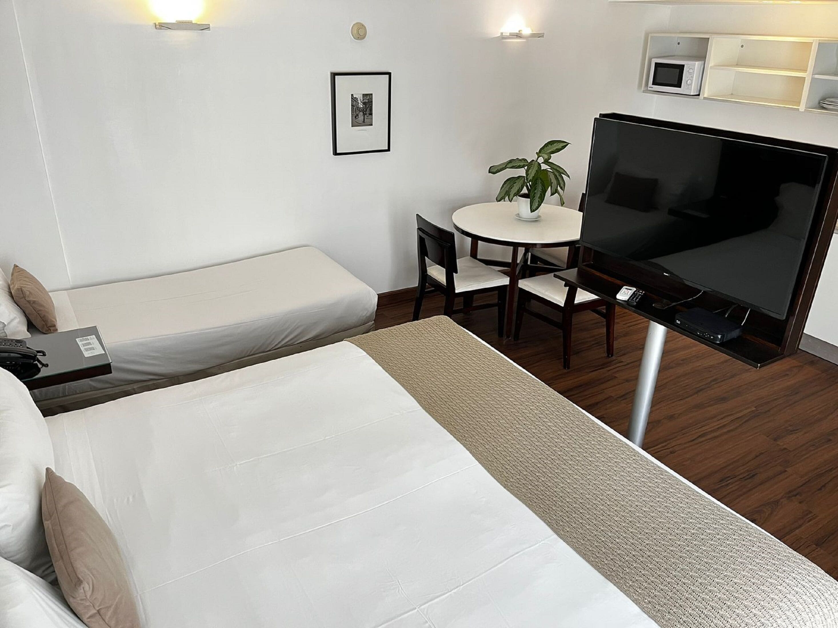 Ett hotellrum med en säng, ett skrivbord med en stol, en tv, en mikrovågsugn och en liten krukväxt.