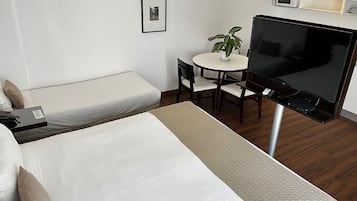 Habitación de hotel con cama, escritorio con silla, televisor, microondas y una pequeña planta en maceta.