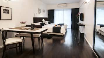 A hotel room with a dining table, two beds, a TV, and a large window with curtains.