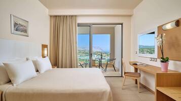 A hotel room with a bed, a desk, a chair, a small table, a potted plant, and a view of the landscape.
