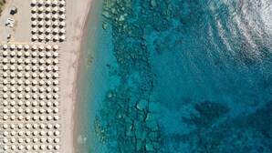 An aerial view of a beach with rows of umbrellas and a rocky shoreline.