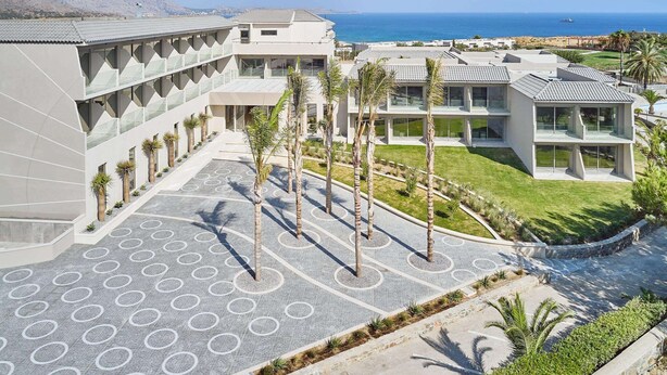 A modern hotel with a spacious courtyard, palm trees, and a view of the ocean.